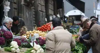 man in brown coat standing in front of fruit stand