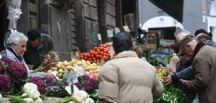 man in brown coat standing in front of fruit stand